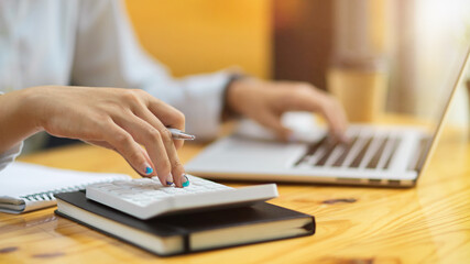 Close up of female accountant fingers using calculator and typing on laptop