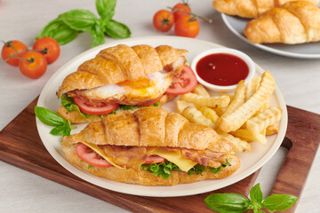 two croissant sandwiches on wooden table, top view, Sandwich with bacon, fried egg. Ham, cheese, bacon, fried egg, tomato, french fries and lettuce served in a plate.
