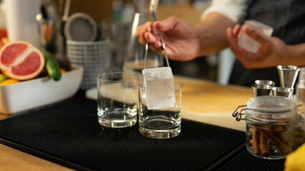 A Bartender Preparing a Glass for a Cocktail by Putting a Big Ice Cube in it Surrounded With...