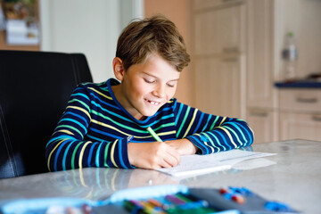 Hard-working happy school kid boy making homework during quarantine time from corona pandemic...