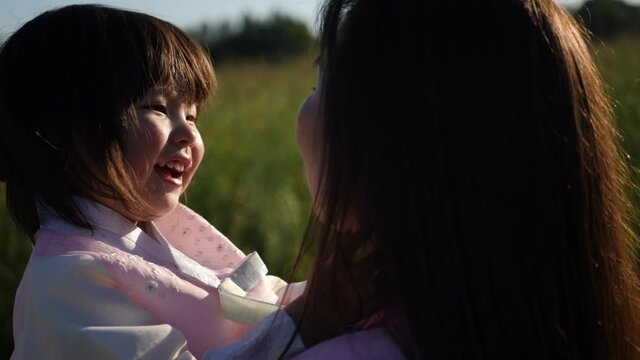koreans family mother and daughter in pink dresses sitting in the long grass