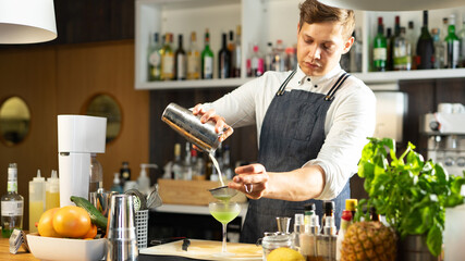 A Caucasian Bartender Preparing a Green Cocktail in a Shaker Surrounded With Bartending Equipment...