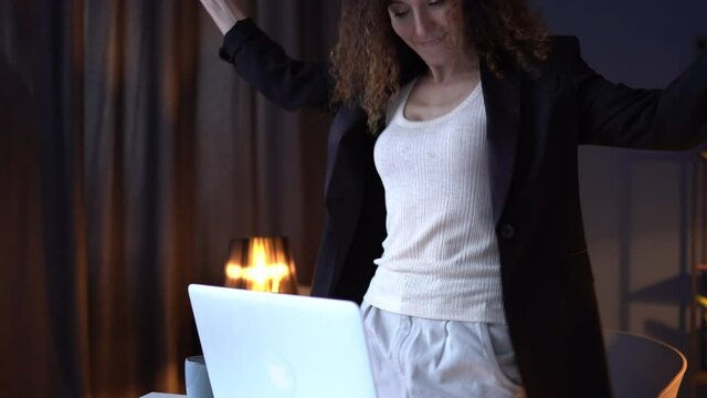 Girl is ancing celebrating the completion of the late work. Happy winner. Beautiful business woman in a business suit is working late in the office