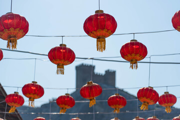 Day, red Chinese traditional beautiful lanterns hang against the background of the blue sky and the fortress from the Middle Ages