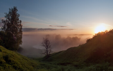 Morning dawn. The sun rises out of the fog over the river