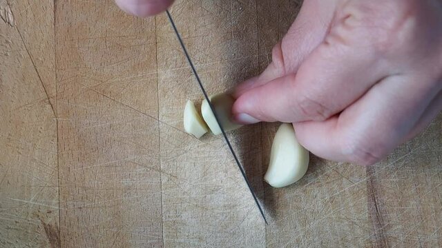 A clove of garlic is cut by a cook on a wooden cutting Board.