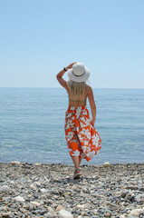 a girl in a white hat and colored skirt stands on the seashore in the summer