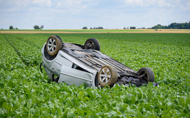 Car turned upside down after accident in a field, a peaceful countryside scenery.