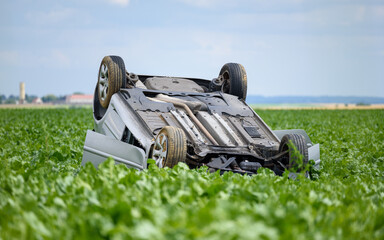 Car turned upside down after accident in a field, a peaceful countryside scenery.