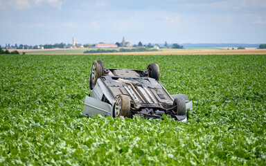 Car turned upside down after accident in a field, a peaceful countryside scenery.