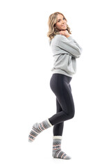 Fototapeta premium Side view of happy young woman in gray hooded sweatshirt posing with raised leg. Full body isolated on white background.