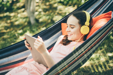 Young girl with smile using tablet on the hammock.