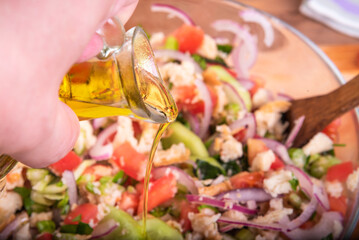 Preparing an authentic Tuscan panzanella salad in a glass bowl. A trickle of olive oil pouring into a bowl of salad.