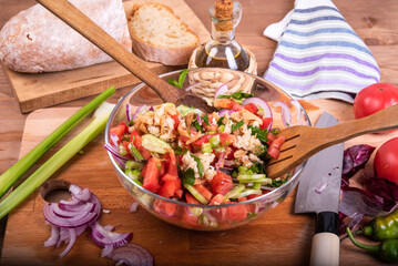 Preparing an authentic Tuscan panzanella salad in a glass bowl. Side view of salad in a bowl on the table with ingredients.