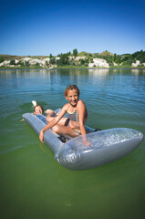 Two little cute girls in swimsuits swim on an inflatable mattress on a blue career lake.