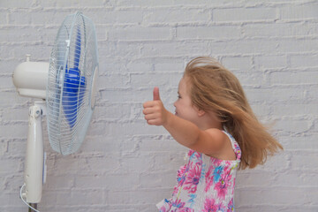 a girl child in front of an electric fan enjoys the flow of cool wind on a hot summer day