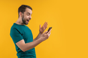 Happy smiling bearded man with smartphone in hands looking surprised winning money after betting online at bookmaker's website using mobile application