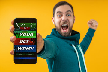 Man being happy winning bet in online sport gambling application on mobile phone, screaming and clencing his his fist - 445341976