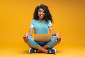 Full length studio portrait of happy smiling drk skinned girl sitting with her laptop computer...