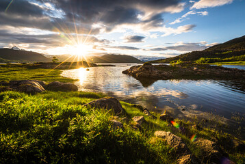 Scenic view of fjord landscape in northern norway with warm midnight sun in late spring with green...
