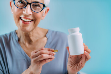 Supplements. Senior woman holding capsule and a blank white supplement container.