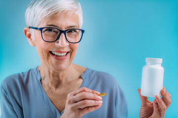 Supplements. Senior woman holding capsule and a blank white supplement container.