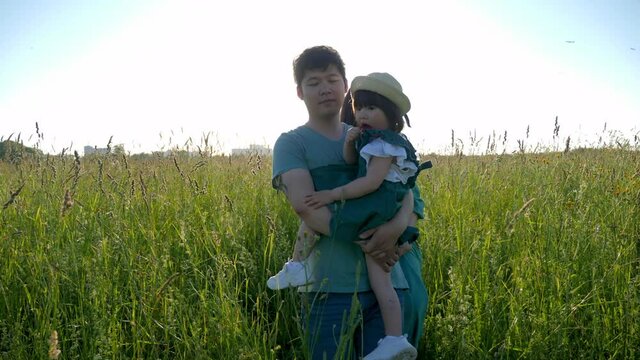 Korean family with their daughter lie in a field in the grass at sunset