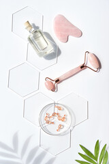 Pink quarts face roller, gua sha stone, serum capsules in chemical glass dish, hexagons, palm...