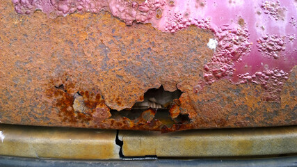 Sheet metal corrosion of old red car. Rusty messy surface. Damaged grunge dirty texture from road salt. Rust background. Protecting the automobile concept. Coat. Copy space. Paint and repair. Hole.