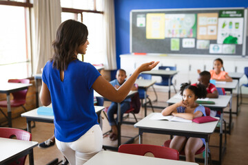 Rear view of african american female teacher teaching students in the class at elementary school - Powered by Adobe