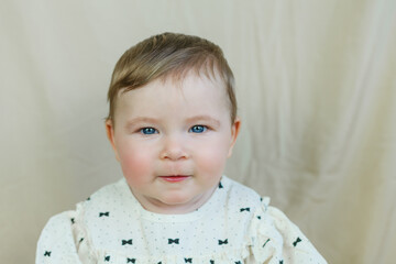 Cute little blue-eyed girl 8 months old on a beige background. Cozy. Home.