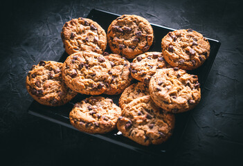 Homemade chocolate chip cookies on a black square plate on a dark table. Ready to eat.