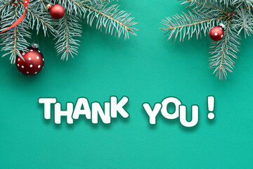 Text Thank you on turquoise Christmas textile background. Top view, flat lay on fir twigs decorated with red glass baubles, traditional Xmas toys.