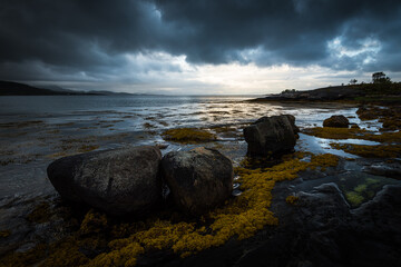 Fjord landscape with rocks in the foreground and dramatic cloudy sky in northern norway during sunset