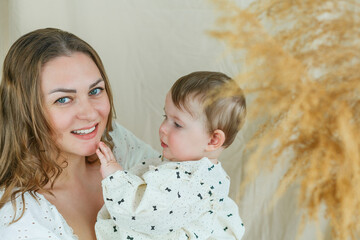 Beautiful young mother with blue-eyed little daughter on a beige background. Cozy.