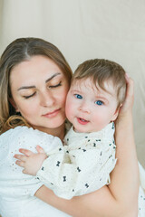 Beautiful young mother with blue-eyed little daughter on a beige background. Cozy.