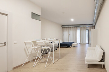 White table with breakfast service prepared with a white sofa bed in the top plan and bedroom in the back in a studio vacation rental apartment.