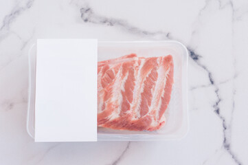Raw pork ribs in vacuum packaging on marble background, logo mockup for design.