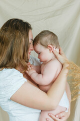 Beautiful young mother with blue-eyed little daughter on a beige background. Cozy.