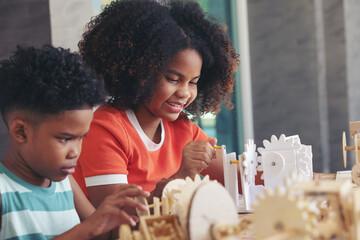 Black boy and girl pay attention to learning the simulation mechanism robot model wooden on table...