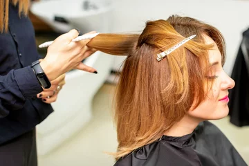 Fotobehang The female client receiving a haircut at the beauty salon, young woman enjoying getting a new hairstyle © okskukuruza