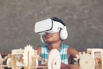 African black boy wearing 3D gadget and looking out above and having the simulation mechanism robot model wooden on table in classroom.