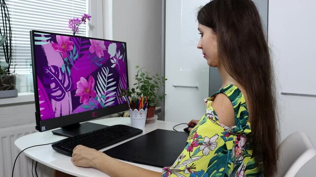 A nice, smiling freelancer, graphic designer, illustrator is working on an illustration, doing digital painting on a graphic tablet. A creative occupation concept.