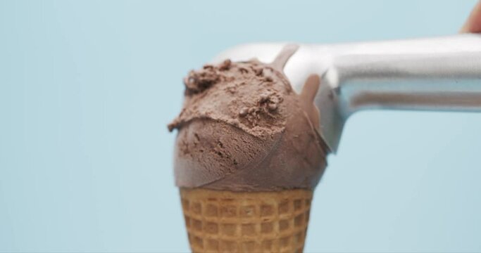 Hand scoop chocolate ice cream waffle cone isolated on blue background, Front view Food concept.