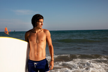 Portrait of handsome surfer with his surfboard. Young man with a surfboard on the beach...