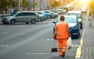 Municipal worker clean up street in the evening. worker in orange uniform collecting garbage from...