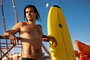 Portrait of handsome surfer with his surfboard. Young man with a surfboard on the beach...