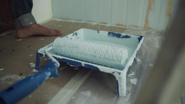 A stream of paint pours into the tray. A bath for painting with a roller. Roller with blue paint. Renovation of the room. Modern interior in the house. Self-isolation. Quarantine. Close up