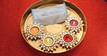 Candles for Diwali festival and a face mask on a tray on a red background