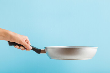 Young adult woman hand holding new aluminium frying pan on light blue background. Pastel color....